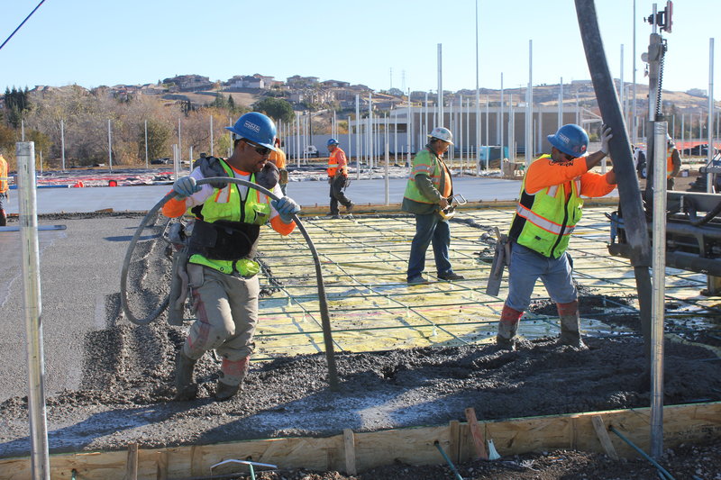 Construction workers with safety vests pouring concrete outside onto wire mesh platform with wood forms as the border