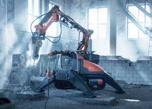 HUSQVARNA DXR DEMOLITION ROBOT drilling in a room filled with dust and light coming in the windows.