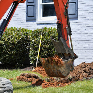 Excavator digging dirt in a lawn by a residential house.