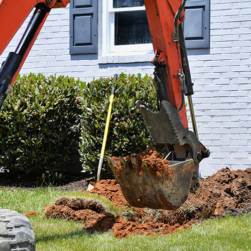 Excavator digging dirt in a lawn by a residential house.