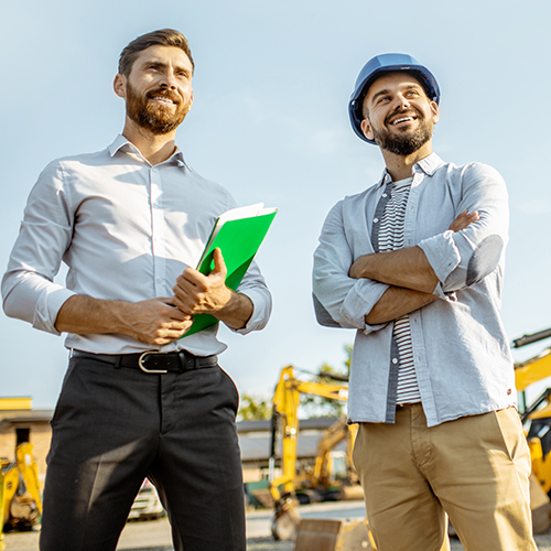 Two men overlooking construction equipment on site during a meeting.
