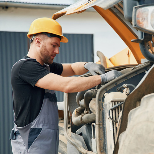 Man Repairing Heavy Equipment on Construction Site. A construction worker repairs a piece of heavy equipment in an outdoor environment during daylight hours.