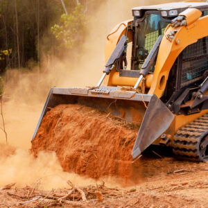 Excavator moves dirt in forested area while creating space for construction work during daylight