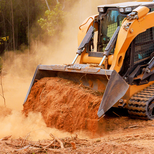 Excavator moves dirt in forested area while creating space for construction work during daylight
