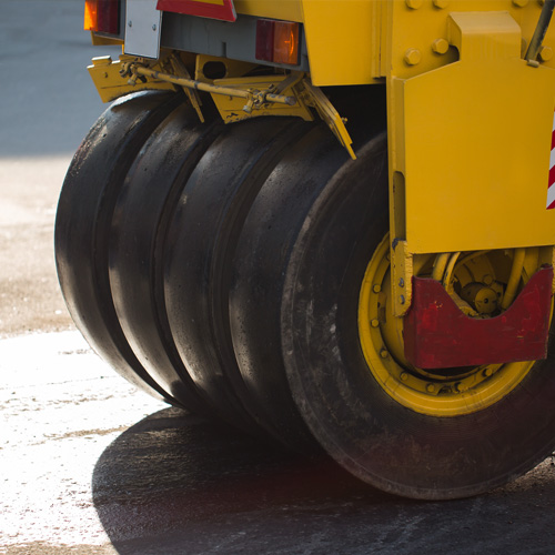 A bright yellow vibrating asphalt roller is seen compacting a new, sleek blacktop surface in this eye-level shot.