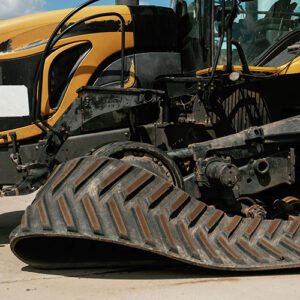 A partially-disassembled black and yellow tractor sits on a concrete surface, with one of its tracks detached and lying nearby.