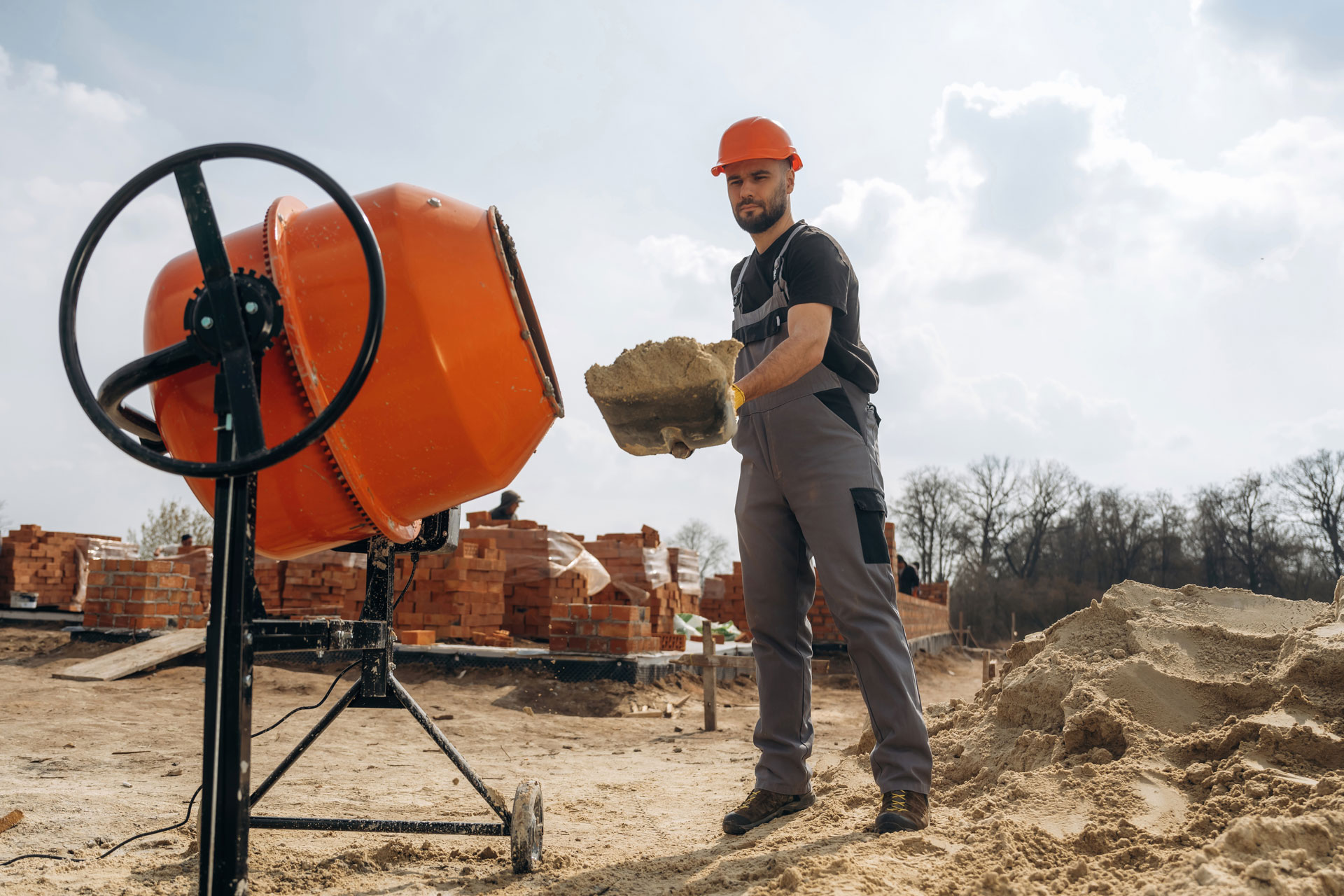 Shovel in hands. Man is working on the construction site with concrete mixer