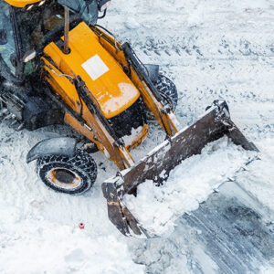Tractor loader machine uploading dirty snow into dump truck. Cleaning city street, removing snow and ice after heavy snowfalls and blizzard. Snowplow outdoors clean pavement sidewalk road driveway.