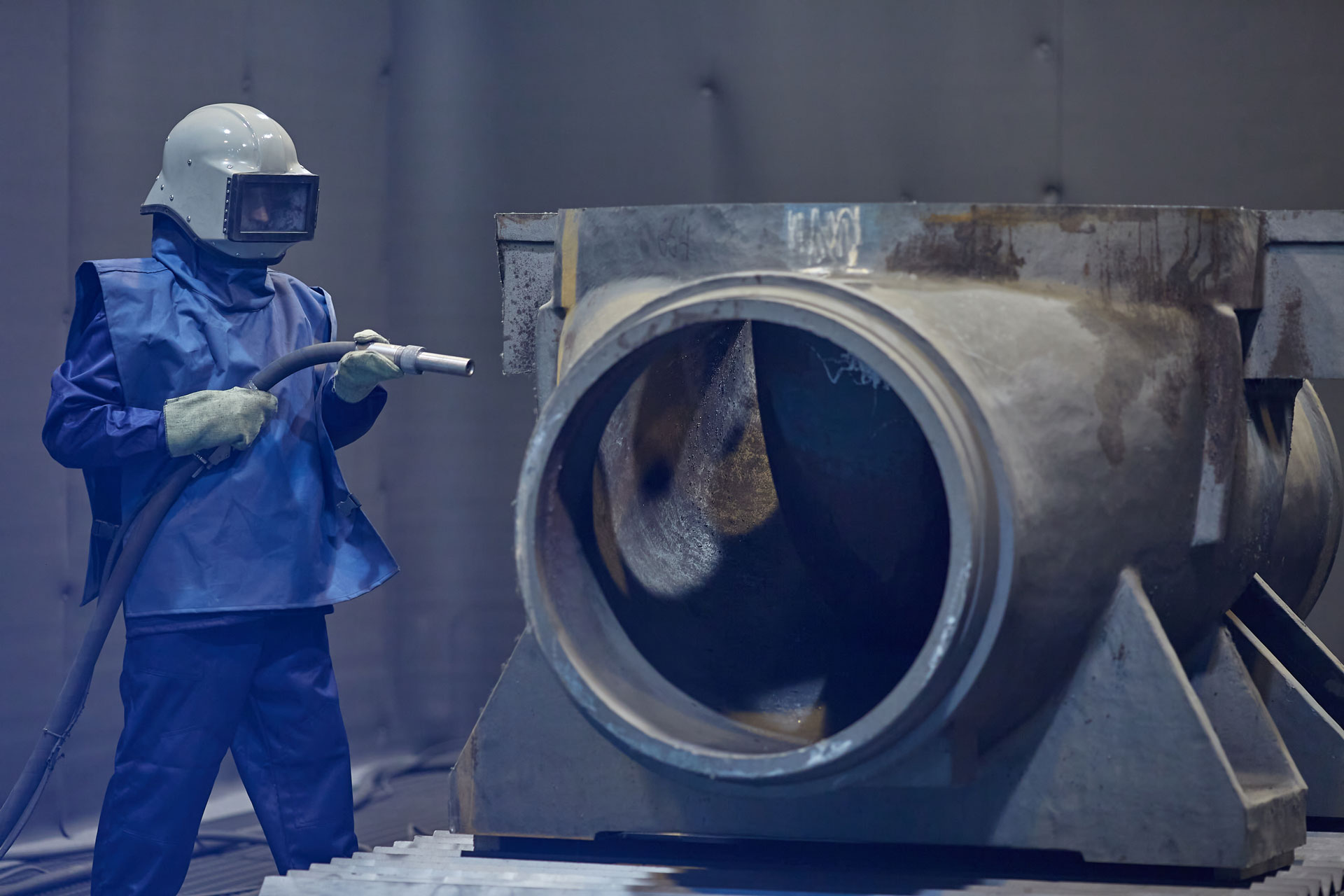 worker processes workpiece with sandblasting tool in factory, selective focus